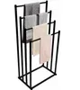 A black metal towel rack with four arms, holding several folded towels of different colors and textures. Produktbild-Vorschau