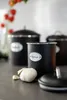 Three black storage containers with silver trim and labels are arranged on a countertop. A garlic bulb and a clove are in the foreground. Produktbild-Vorschau