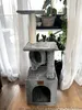 A multi-level cat tree with scratching posts and a hideaway, placed indoors near a window with sheer curtains. Náhled obrázku produktu