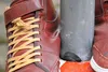 A close-up view of two brown leather shoes with yellow laces, positioned next to a gray pole. Produktbild-Vorschau