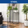 Two black metal plant stands with plants on them, placed in a room with sheer curtains and wooden flooring. Anteprima dell’immagine prodotto