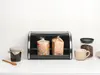 A black bread bin with two items inside, a jar of jam and a wooden spoon to the left, and a mug and jar of coffee beans to the right. Podgląd zdjęcia produktu