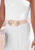 A woman wearing a white dress and a beige and gold belt, holding a straw bag. Produktbild-Vorschau