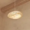 A woven bamboo pendant light hangs from the ceiling, illuminated from within, against a textured wall and wooden beam. Podgląd zdjęcia produktu