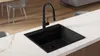 A black kitchen sink with a black faucet is shown on a white countertop. Produktbild-Vorschau