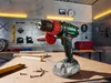 A cordless impact drill is placed on a workbench in a workshop setting, surrounded by tools and wood. Produktbild-Vorschau