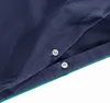 Close-up of a dark blue fabric with green trim and two silver snap fasteners. Anteprima dell’immagine prodotto