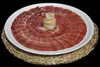 A plate of thinly sliced ham arranged in a circular pattern, with a decorative piece of fat in the center, placed on a woven mat. Produktbild-Vorschau
