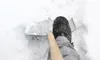 A person is shoveling snow with a shovel, wearing winter boots. Voir les images du produit