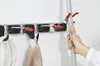 A hand is shown holding a broom or mop handle, about to place it onto a wall-mounted storage rack. Anteprima dell’immagine prodotto