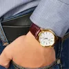A close-up shot of a person's wrist wearing a gold watch with a brown leather strap, with a wallet tucked into their jeans pocket. Anteprima dell’immagine prodotto