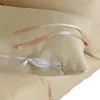 A close-up view of a beige cushion with a zipper and two ribbon ties. Produktbild-Vorschau