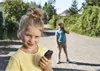 Two children are standing on a paved path outdoors, one in the foreground holding a walkie-talkie and the other in the background talking on a phone. Produktbild-Vorschau