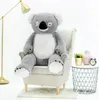 A large plush koala bear sits in an armchair next to a small side table with decorative items. Náhľad obrázku produktu