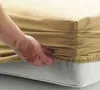 A hand is shown tucking a beige fitted sheet onto a mattress. Produktbild-Vorschau