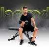 A man is performing bicep curls with a dumbbell while sitting on a black adjustable weight bench. The background features a dark, smoky gradient with bright yellow text that reads 'Jacked'. Náhľad obrázku produktu