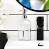 A clear glass soap dispenser with a black faucet on a white sink. Náhled obrázku produktu