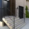 A black metal handrail is installed on a set of outdoor concrete stairs leading up to a building entrance. Produktbild-Vorschau