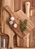 Several wooden cutting boards are arranged on a wooden surface. Some garlic and herbs are placed on one of the boards. Podgląd zdjęcia produktu