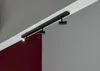 A black track light fixture with three spotlights mounted on a white ceiling track, angled towards a corner where two walls meet. One spotlight is illuminated. Náhľad obrázku produktu
