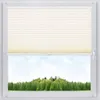 A window with a cream-colored pleated blind partially covering the view of a green forest and blue sky. Produktbild-Vorschau