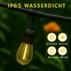 A close-up of a string light bulb with water droplets on it, hanging from a black cable outdoors. Produktbild-Vorschau