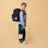 A young girl wearing a backpack and jeans stands against a plain background. Produktbild-Vorschau