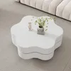 A white, flower-shaped coffee table on a gray carpet, next to a section of a cream-colored sofa. A small angel figurine and a vase with greenery are on the table. Voir les images du produit