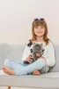 A young girl sitting on a couch holding a stuffed animal. Voir les images du produit