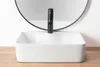 A white rectangular vessel sink with a black faucet is shown in front of a round mirror. Náhled obrázku produktu