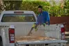 A man is using a leaf blower to clean out the bed of a white pickup truck. Produktbild-Vorschau