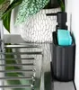 A black soap dispenser with a blue sponge sits next to a kitchen sink, with a potted plant in the background. Produktbild-Vorschau