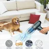 A golden retriever dog lies on a white carpet next to a sofa, while a hand holds a portable vacuum cleaner that is shown sucking up pet hair, bread crumbs, cigarette ash, and dust particles. Produktbild-Vorschau
