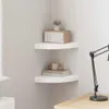 Two white corner shelves are mounted on a light gray wall. The top shelf holds a wooden radio and a small potted plant. The bottom shelf holds a stack of books with a mug and a small wooden cat figurine on top. A black desk lamp is visible on the right sid Voir les images du produit