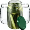 Three glass jars are shown, one filled with pickles and brine, and two empty. A green lid is placed in front of the filled jar. Podgląd zdjęcia produktu