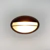 A close-up, front-facing view of an oval-shaped outdoor wall light with a bronze-colored metal casing and a frosted white light diffuser. Podgląd zdjęcia produktu