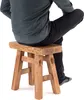 A person is sitting on a wooden stool. Produktbild-Vorschau