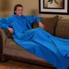 A woman is sitting on a couch, wrapped in a large blue blanket with sleeves. Náhľad obrázku produktu
