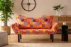 A colorful patchwork sofa is shown in a living room setting, with a plant and a cabinet in the background. Produktbild-Vorschau