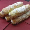 A close-up shot of several cream-filled pastries dusted with powdered sugar, arranged on a red napkin. Produktbild-Vorschau