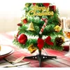 A mini Christmas tree decorated with ornaments and a 'Merry Christmas' sign, placed on a table with festive decorations. Náhled obrázku produktu