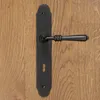 A black door handle with a long backplate is mounted on a wooden door. Produktbild-Vorschau