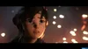 A close-up of a young girl's face, looking upwards with a concerned expression. The background is dark and out of focus, with numerous glowing orange and white orbs, suggesting a scene of fire or sparks. Produktbild-Vorschau