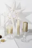 A festive Christmas decoration featuring a large paper star and three lit candles on a white surface. Voir les images du produit