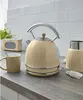 A cream-colored retro electric kettle and matching mug are on a countertop, with a retro radio and a blender in the background. The scene is set against a white subway tile backsplash. Podgląd zdjęcia produktu