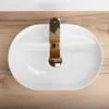 A top-down view of a white oval sink with a gold faucet, placed on a wooden surface. Náhled obrázku produktu