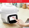 A hand is shown interacting with the touchscreen of a smart multicooker on a wooden countertop, with kitchen items in the background. Voir les images du produit