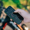 A person is holding a smartphone with a cycling app open, outdoors. Produktbild-Vorschau
