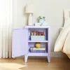 A purple nightstand with its door open, placed next to a bed. The nightstand contains books, a decorative vase, and some packaged snacks. Náhľad obrázku produktu