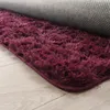 A close-up view of a plush, shaggy rug with a deep purple color, partially rolled up to reveal its grey backing and the light wood floor beneath. Voir les images du produit